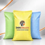 Três sacos de ráfia coloridos (verde, amarelo e azul) com a marca Sandra Embalagens impressa no saco amarelo central.