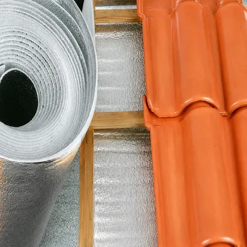 Manta térmica aluminizada refletiva em rolo instalada sob telhado de cerâmica, utilizada para isolamento térmico e conforto em coberturas residenciais e comerciais.